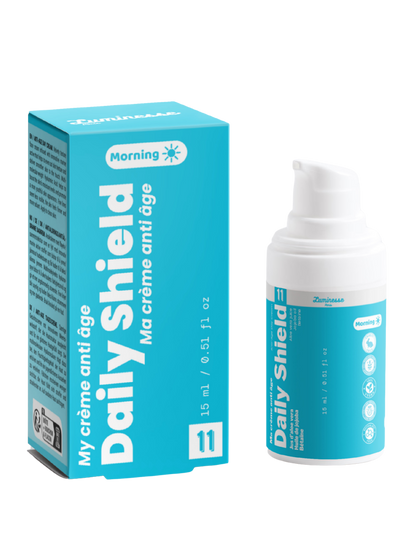 Packshot de Daily Shield n°11 de Luminesse Paris avec son étui turquoise et son flacon pompe blanc de 15 ml. La boîte et le flacon sont présentés côte à côte sur fond transparent ; le packaging indique une crème anti-âge pour le matin et mentionne notamment jus d’aloe vera, huile de jojoba et bétaïne.