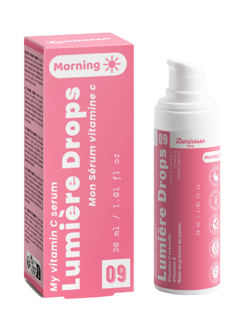 Packshot de Lumière Drops n°09 de Luminesse Paris avec son étui rose et son flacon pompe blanc de 30 ml. Le produit et la boîte sont présentés côte à côte sur fond transparent ; la mention Morning ainsi que les références à la vitamine C, vitamine E et huile de graines de jojoba sont visibles.